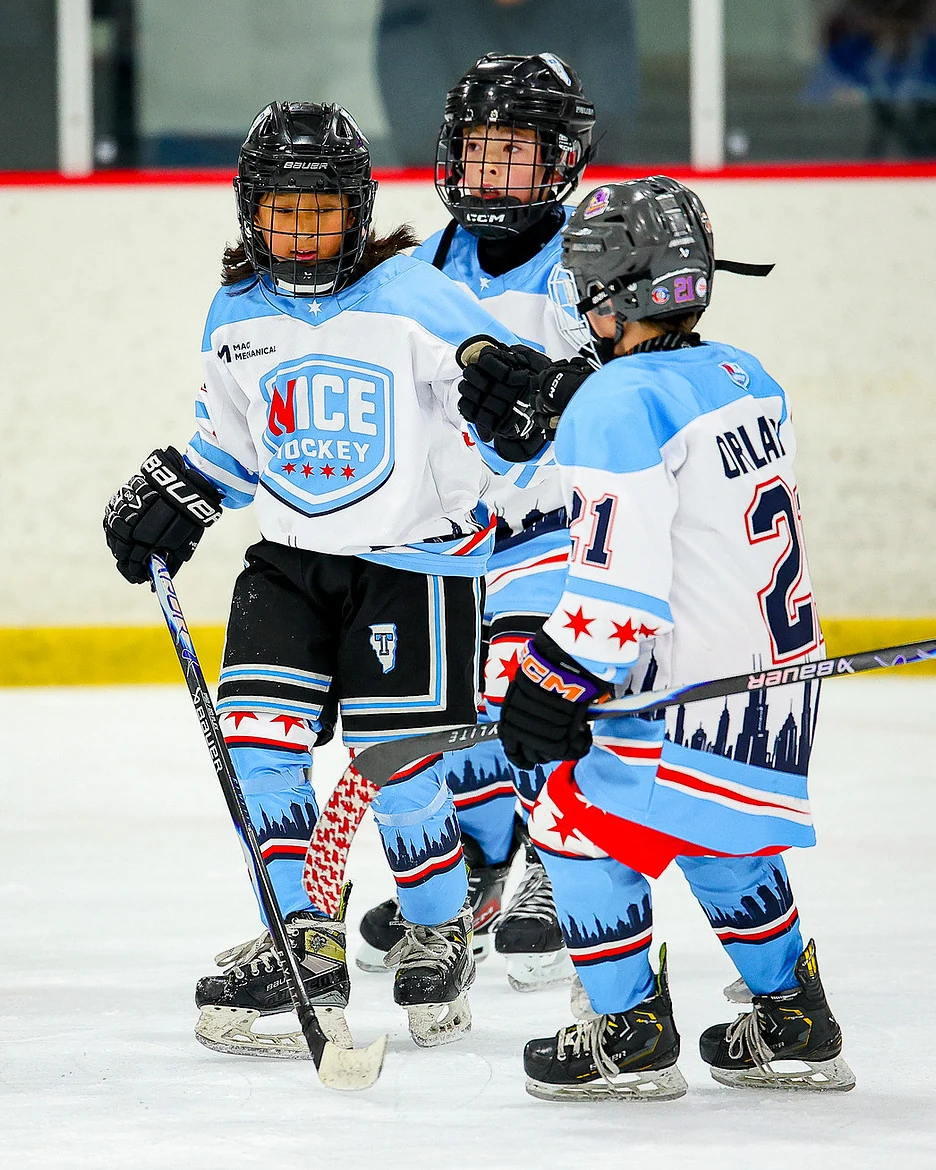 NICE Hockey teammates together on the ice in light blue, white and red uniforms